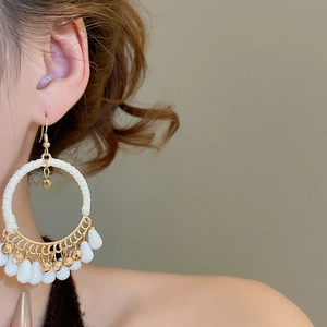 Detail of bohemian gold hoop earrings with white woven thread and dangling teardrop beads