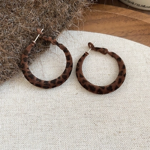 Détail de créoles floquées à motif léopard sur un présentoir en lin et bois
