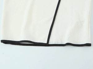 Detailed close-up of white crepe top hem with black contrast trim and woven texture