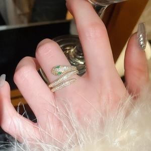Detail of a gold plated snake ring with pavé crystals and green gem eyes on a finger