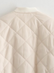 Détail du matelassage en losanges et du col en maille côtelée sur la veste crème