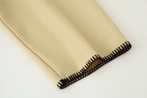 Detailed close-up of beige suede fabric with black decorative hand-stitched embroidery edge