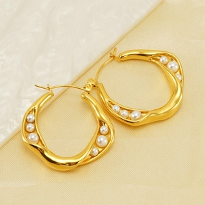 Detailed view of wavy gold-plated hoop earrings with irregularly embedded white pearls