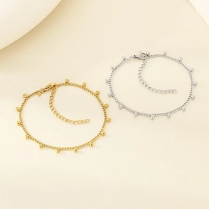 Detail of gold and silver chain bracelets with polished bead charms on a textured background