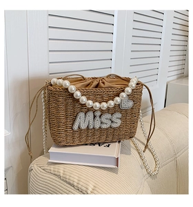 Detail of woven straw bag with pearl handle and sparkling MISS rhinestone letters