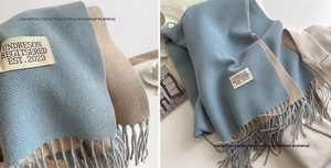 Detail of soft cashmere-feel scarf with fringes and woven brand label in blue and beige