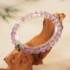 Detailed view of amethyst beaded bracelet on wood stand with silver hollow charm