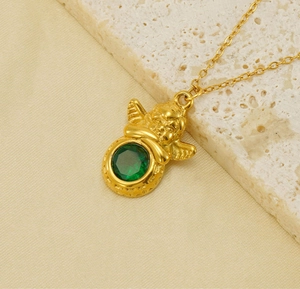 Gros plan d'un collier pendentif ange doré avec une pierre précieuse verte brillante