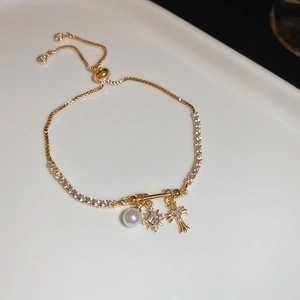 Detail of adjustable gold bracelet featuring zircon cross, star and pearl charms