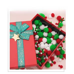 Christmas gift box with red green white pom-poms, festive ribbon and warm LED fairy lights
