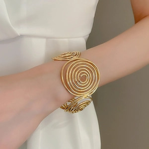 Detailed close-up of a large golden spiral wave cuff bracelet on a female wrist