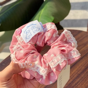 Detailed close-up of pink heart-patterned hair scrunchie with white lace and floral tag