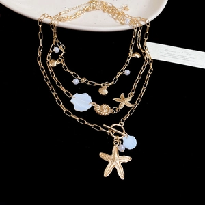Detail of layered gold necklace with starfish, shell charms and white pearls on dark background