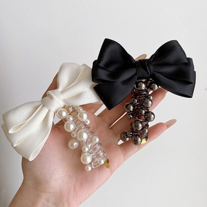 Detailed close-up of bow knot hair ties with pearls and spiral cord shown in hand