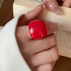 Detail of a glossy red resin geometric square ring worn on a model's hand with a book