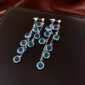 Detail of silver drop earrings with blue crystals and long tassels on silk background