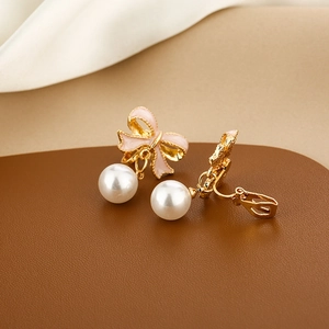 Detail shot of pink enamel bow earrings with dangling pearls on textured leather