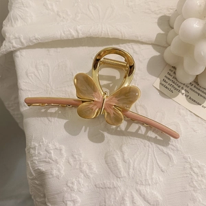 Close-up of golden butterfly hair claw with pink enamel details on lace fabric