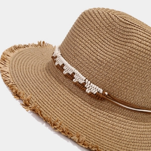 Detailed macro of handwoven straw hat showing fringe brim and decorative braided rope