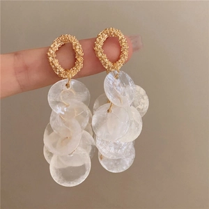 Macro detail of gold stud earrings featuring cascading white shell tassels and ring