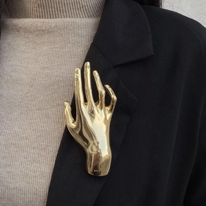 Detailed view of a gold metallic hand-shaped brooch on a black blazer lapel accessory