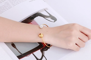 Détail d'un bracelet jonc doré en forme de C avec une boule en or poli et une boule pavée de cristaux