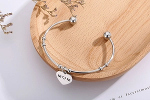 Détail d'un bracelet en acier argenté avec pendentif cœur gravé MOM pour la Fête des Mères