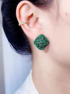 Macro shot of geometric green rhinestone stud earrings and gold ear cuff on a model