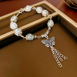Vue macro du pendentif papillon et perles marbrées sur un bracelet à pompons argenté