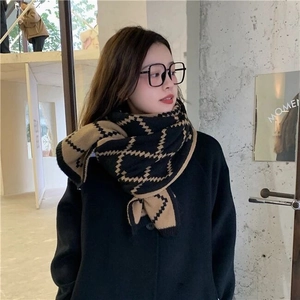 Close-up of model wearing a stylish black and camel checkered knit scarf in a cafe
