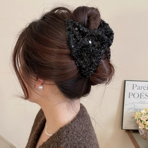 Close-up of a sparkling black sequin bow hair claw clip worn on a woman's bun