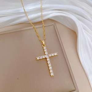 Gold-plated cross pendant necklace with sparkling cubic zirconia on a beige silk surface