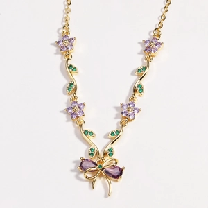 Elegante goldene Halskette mit lila Pfirsichblüte und Kristallschleife auf weißem Grund
