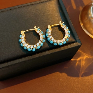 Macro detail of 18k gold plated turquoise and diamond hoop earrings on a black jewelry box