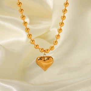 Detailed view of gold beaded chain necklace with heart pendant on soft silk background