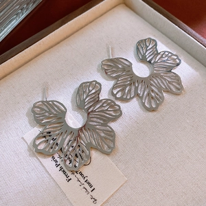 Macro shot of silver hollow-out flower stud earrings on an elegant textured jewelry box