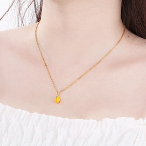 Detail of a gold stainless steel necklace with a vibrant yellow fruit pendant on model
