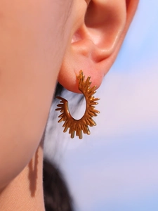 Detailed view of sunburst gold earring with spiked wave design on model's ear