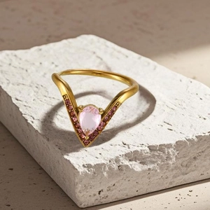 Détail macro d'une bague en V dorée avec pierre poire rose sur un socle en pierre