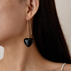 Close-up of elegant gold heart earrings with black glossy pendant worn by a model