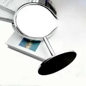 Close-up of dual-sided chrome vanity mirror with rotating metal stand on books
