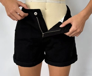 Dettaglio della cerniera in metallo e trama denim su pantaloncini neri a vita alta
