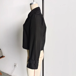 Détail de la manche d'un trench court noir avec sangle de poignet réglable sur mannequin
