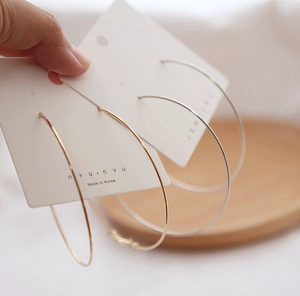Close-up of gold and silver large metal hoop earrings on a minimalist display card