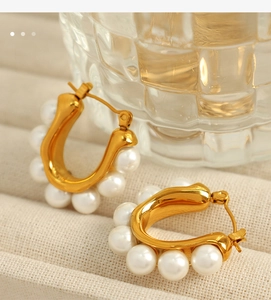 Macro shot of U-shaped gold earrings with five pearls on textured beige fabric