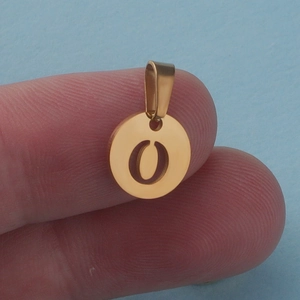 Detail of golden stainless steel round charm with hollow letter O held on finger