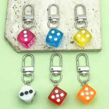 Close-up of six colorful acrylic dice keychains on a stone surface with green background