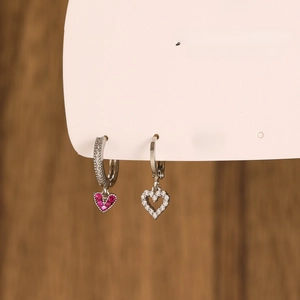 Macro shot of silver heart earrings set featuring red and white zircon stones on a wooden background
