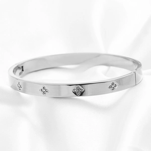 Detail van zilveren armband met gegraveerde klavers en kristallen op witte zijde
