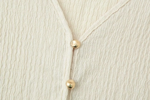 Detail of cream-colored textured V-neck top featuring elegant gold spherical buttons